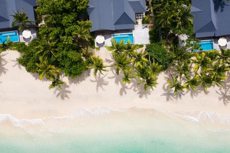 An aerial view of several of Kokomo’s beachfront villas nestled in amongst lush tropical vegetation with the wide, pristine sandy beach extending out from each villa’s deck towards the clear turquoise ocean.