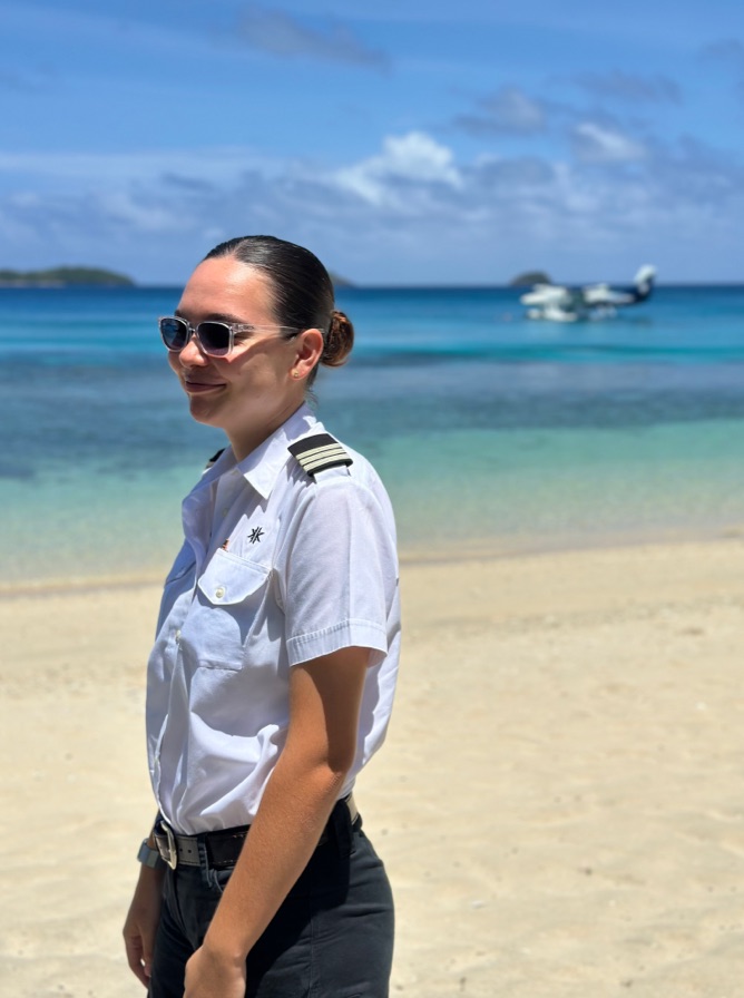 Cynthia standing on the beach at Kokomo Private Island with the seaplane in the background on the water.