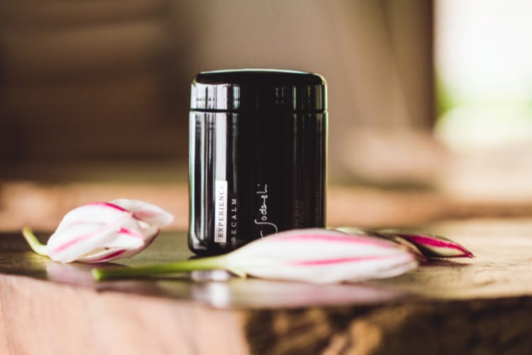 A glossy black Sodashi beauty product on a thick, wooden table, with several flower buds arranged around it on the tabletop.