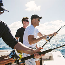 Three people on a deep sea fishing boat off the coast of Kokomo Private Island Fiji reeling in a fish.