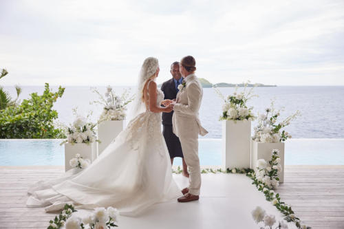 A newly wedded couple looking at the marriage celebrant whilst standing on the deck at of one of the private residences at Kokomo Private Island.