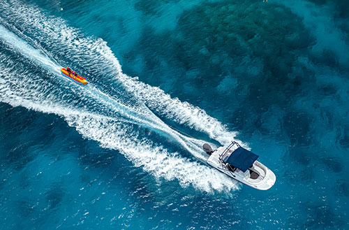 Aerial view of a speedboat towing a yellow inflatable tube with two people on a vibrant blue ocean at Kokomo Island Fiji