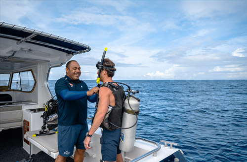 A Kokomo Island Fiji staff member helping a guest get fitted with scuba gear