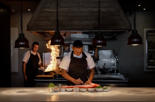 Two chefs in one of the kitchens at Kokomo Private Island Fiji preparing and cooking food.