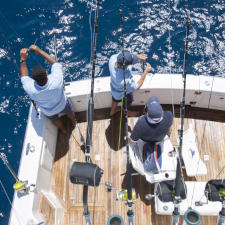 A bird's-eye view of the tail end of a fishing boat with 3 people preparing tackle and bait on large fishing lines.