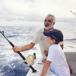 A bird's-eye view of the tail end of a fishing boat with 3 people preparing tackle and bait on large fishing lines.