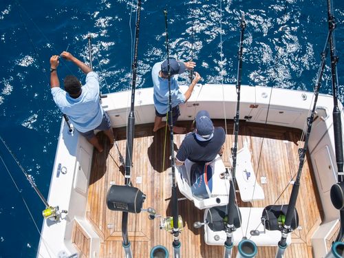 A bird's-eye view of three people at the stern of one of the Kokomo Island Fiji fishing boats preparing tackle and bait on the end of their large fishing lines.