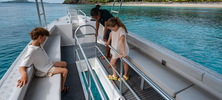 Two kids with one of the staff at Kokomo Island Fiji looking down through the glass bottom boat 'Nemo'