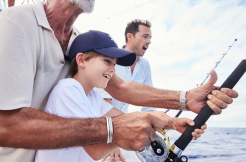 A young boy and man reeling in a fish on the back of a boat off the shore of Kokomo Private Island Fiji.