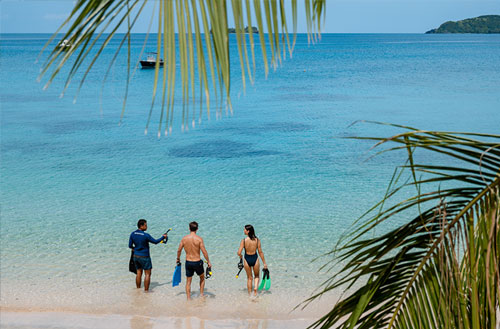 A couple walking and a Kokomo team member walking into clear blue water about to go snorkelling