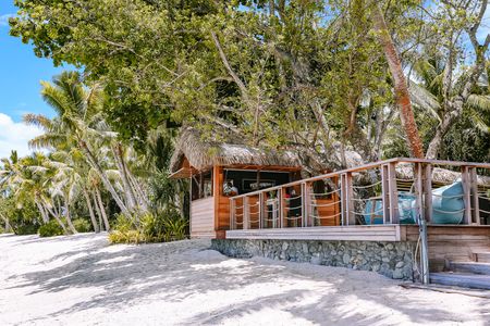 A small thatched-roofed bar with a walk-up beachfront bar and adjoining deck area nested in amongst palm trees.