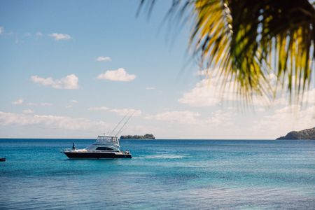 One of Kokomo’s offshore fishing boats slowly cruising across the calm ocean towards the Kokomo jetty, with a small nearby island visible on the horizon.