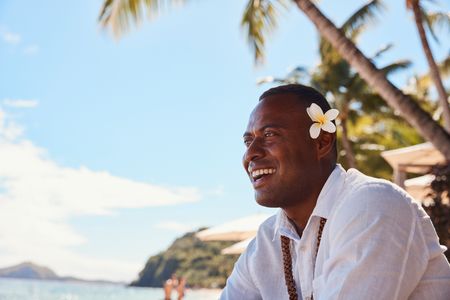 A smiling staff member looking out over the beach at Kokomo Island Fiji, with a large white flower tucked behind their ear.
