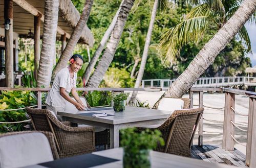 A smiling staff member setting a table on a dining deck area at Kokomo Private Island Fiji.