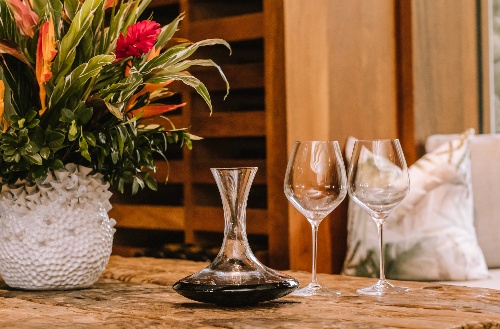 Wine glasses and jug next to flowers in large vase on a table at the wine cellar at Kokomo Private Island Fiji.