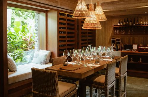 Wine glasses and jug next to flowers in large vase on a table at the wine cellar at Kokomo Private Island Fiji.