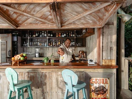 A bartender pouring a cocktail into a martini glass at Walker D'Plank’s wooden bar at Kokomo Private Island Fiji.