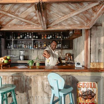 A bartender pouring a cocktail into a martini glass at Walker D'Plank’s wooden bar at Kokomo Private Island Fiji.