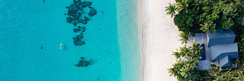 An aerial view of the beachfront villas and nearby reefs at Kokomo Island Fiji.