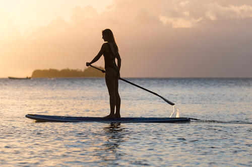 A guest stand-up paddleboarding in front of the sunset in the waters surrounding Kokomo Private Island Fiji